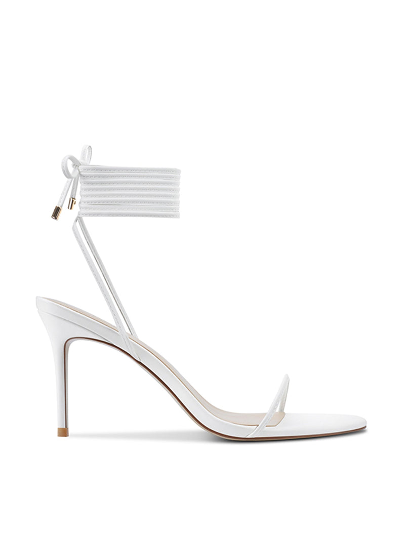 FEMME LA 3.0 Barely There Lace Up Heel in white — side profile showing thin toe strap, slim stiletto heel, and multi-wrap lace-up ankle cuff with gold aglets