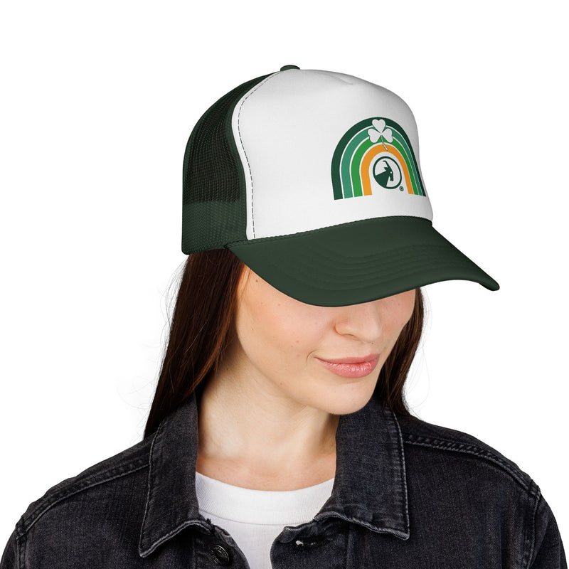 Woman wearing a green and white cap with rainbow and clover, smiling on a white background