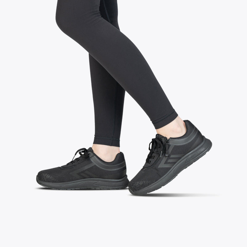 A person wearing Black to the Floor BILLY Sport Inclusion shoes from BILLY Footwear and black leggings stands on a light gray background, with only their legs and feet visible.