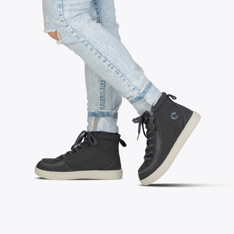 A person wearing light blue ripped jeans and Charcoal/White BILLY Classic Lace High sneakers from BILLY Footwear stands against a plain white background.