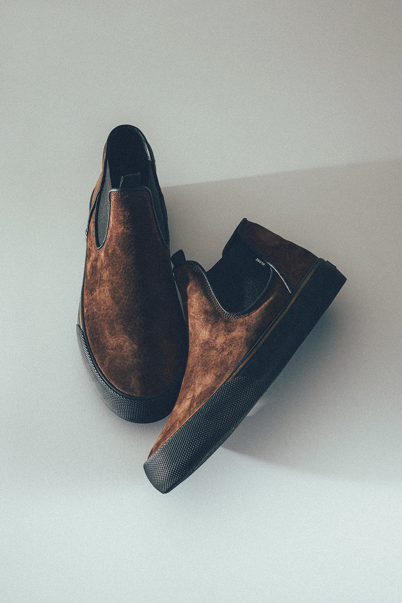 Brown suede Chelsea boots with black sole and elastic side panels displayed on a light background.
