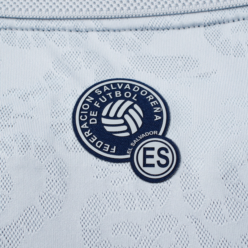 Round ES El Salvador badge on light grey patterned football jersey