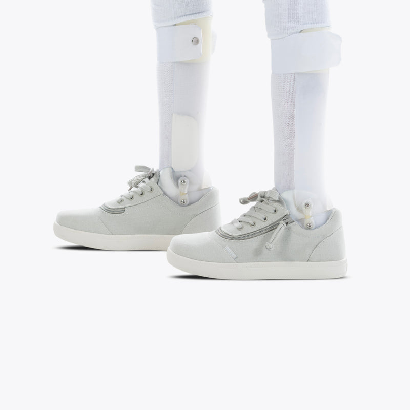 A pair of FINAL SALE - Grey BILLY D|R Short Wrap Low Tops by BILLY Footwear, designed for AFO use and worn on prosthetic legs with white socks, displayed against a plain white background.