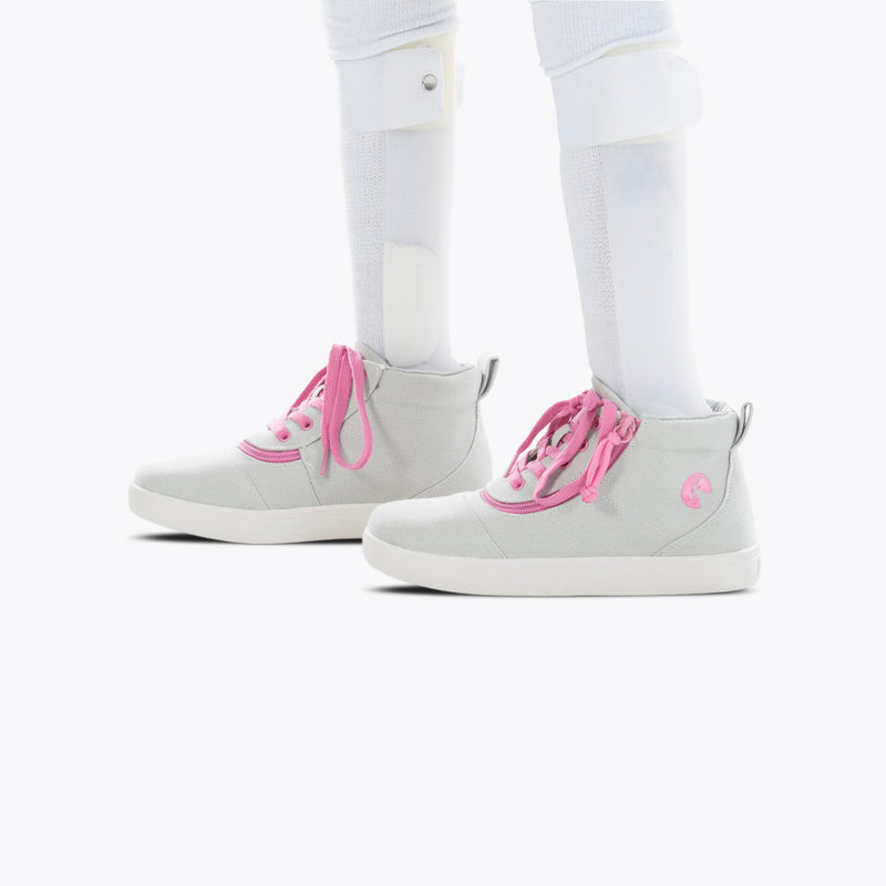 A person with white orthotic leg braces and socks stands in FINAL SALE - Grey/Pink BILLY D|R Short Wrap High Tops by BILLY Footwear, featuring pink laces and trim, against a white background.