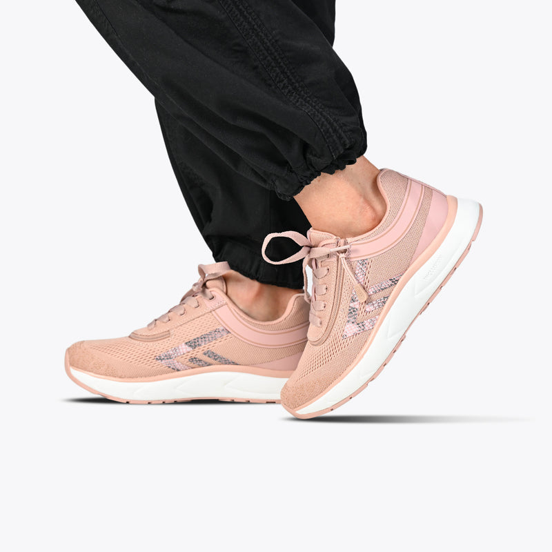 Close-up of a person wearing the FINAL SALE - Women's Pink/Exotic BILLY Sport Inclusion sneakers by BILLY Footwear, featuring mesh details and patterned stripes, styled with black joggers against a plain white background.