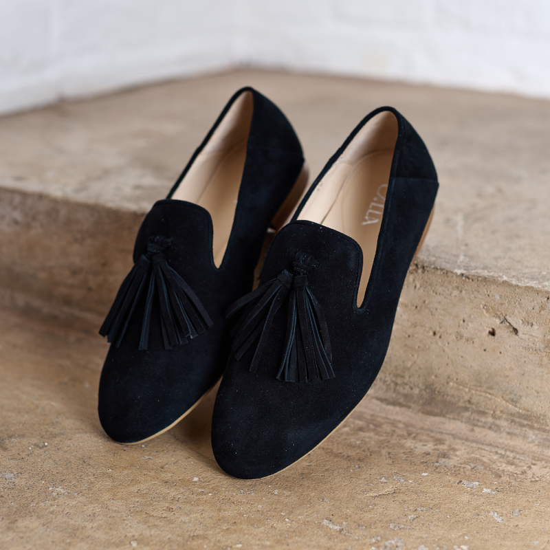 Pair of black loafers with tassels on a textured surface