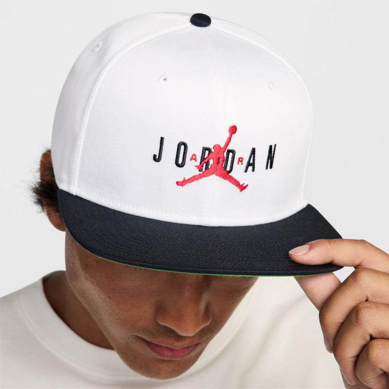 White snapback cap with red Jumpman logo; dark bill and green underbill