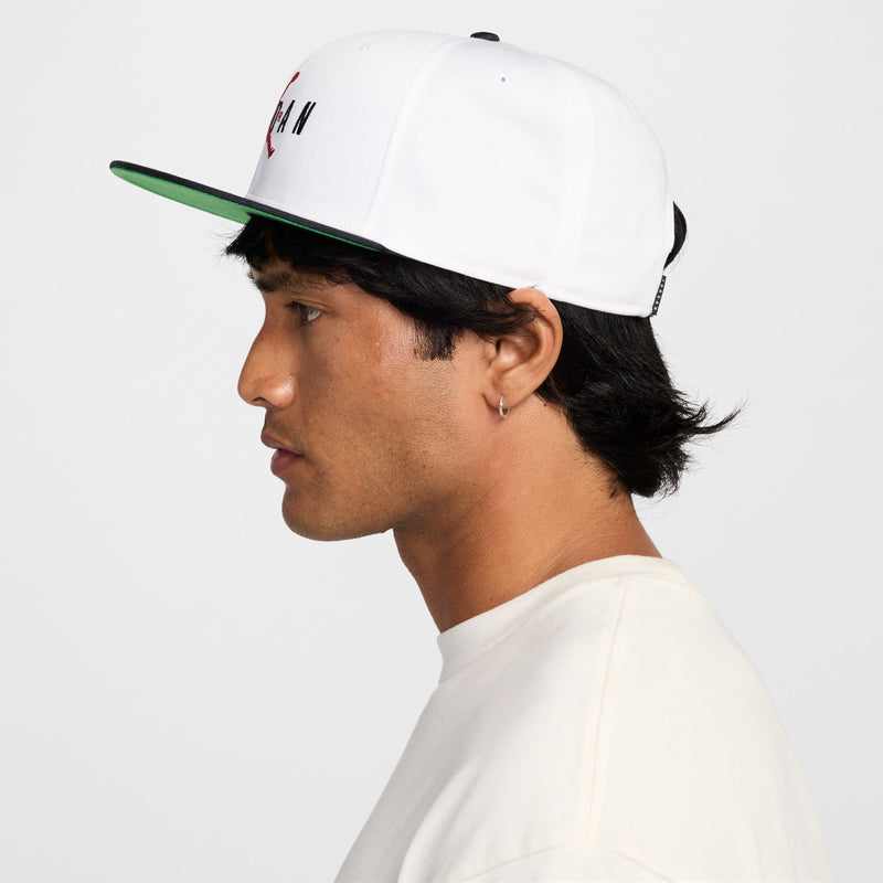 White snapback cap, side view; green underbill and red Jumpman logo