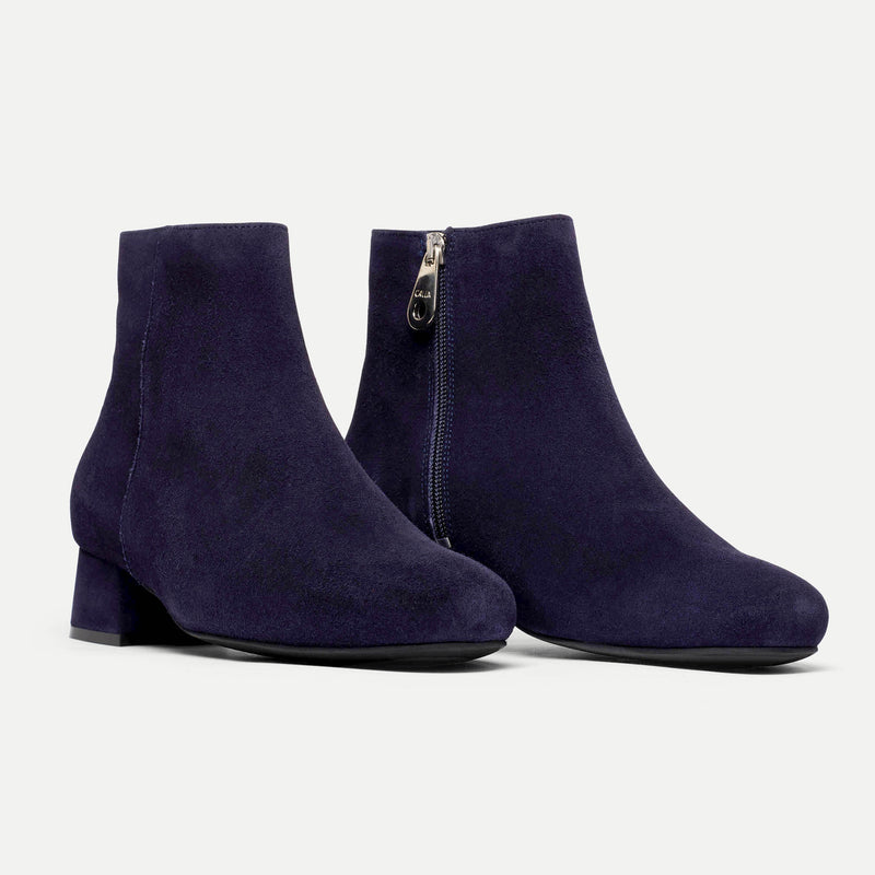 Pair of navy blue ankle boots with a zipper on a light gray background