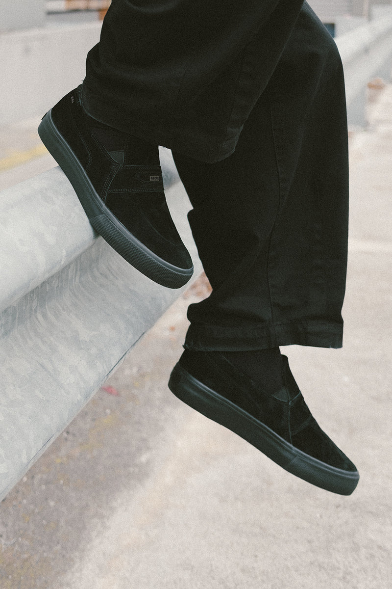 Side view of black Liaizon slip-on skate shoe worn with dark pants