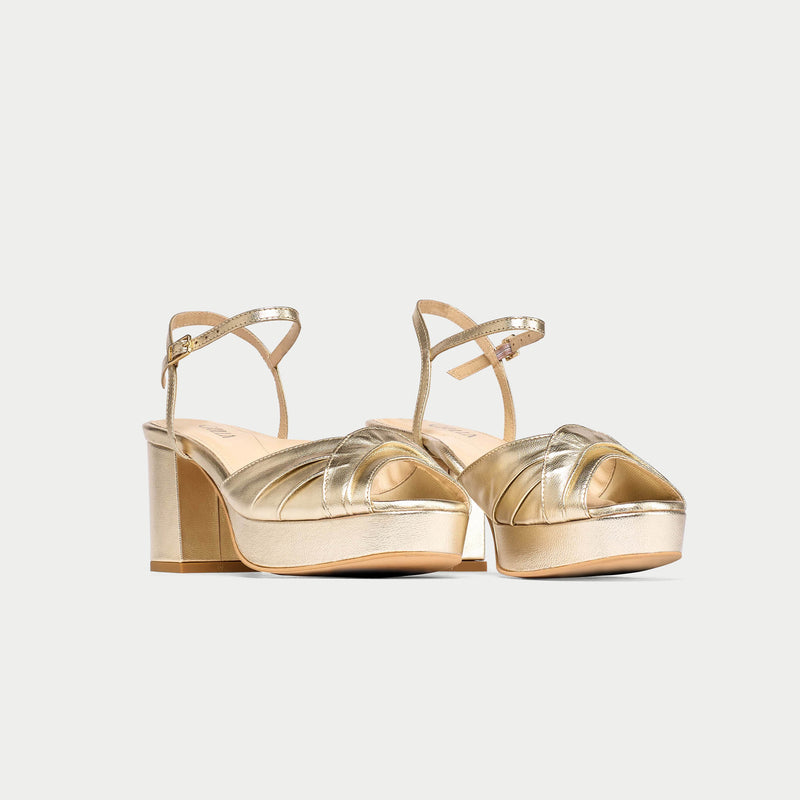 Gold high-heeled sandals on a light gray background