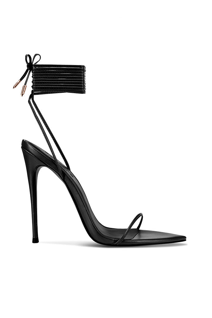 FEMME LA Luce Minimale in black — side profile of black stiletto sandal with thin toe strap and multi-wrap lace-up ankle cuff tied in a bow with gold aglets