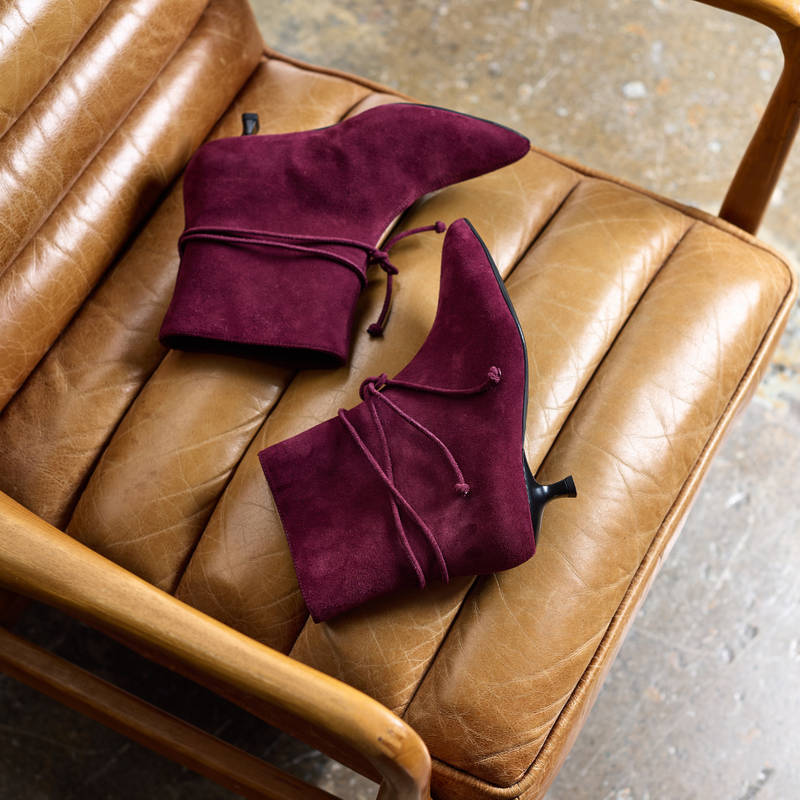 Pair of maroon suede shoes on a brown leather chair.