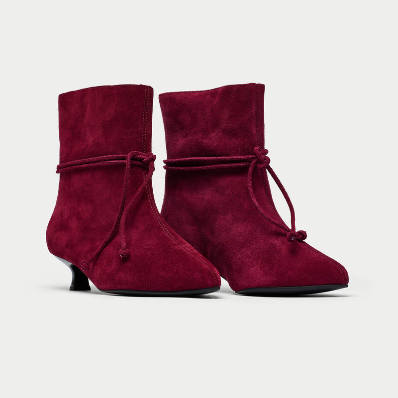 Pair of maroon ankle boots with tied design on a light gray background
