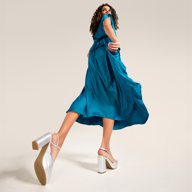 Woman in a blue dress with silver shoes on a beige background
