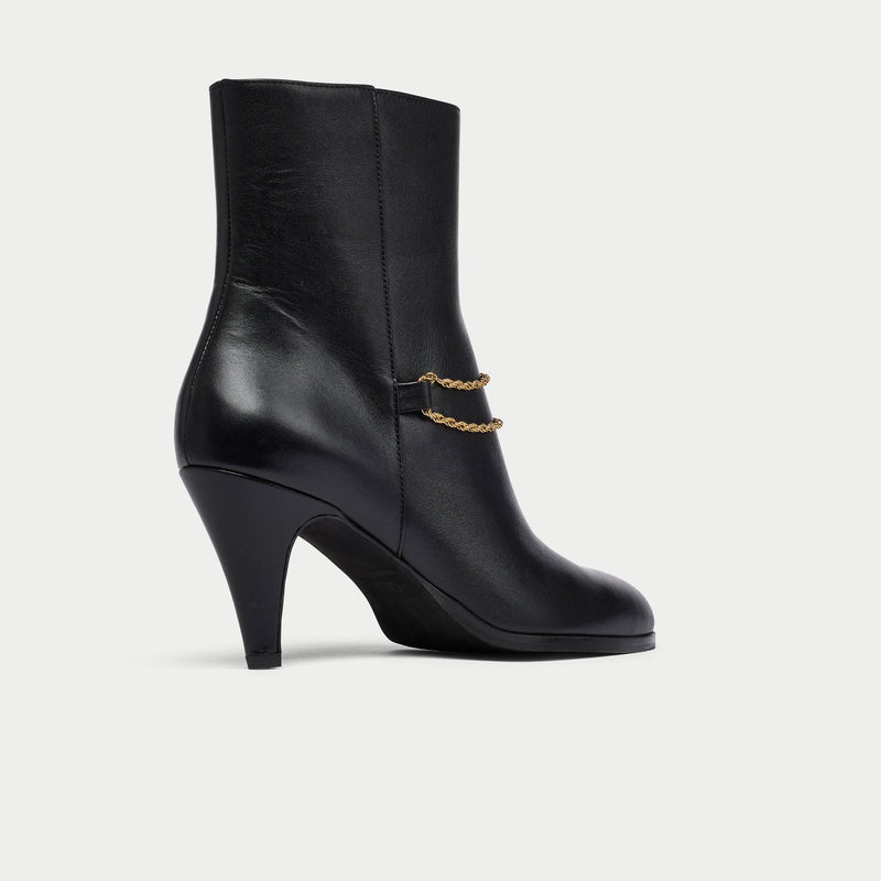 Black Maya ankle boot with a gold chain on a light gray background