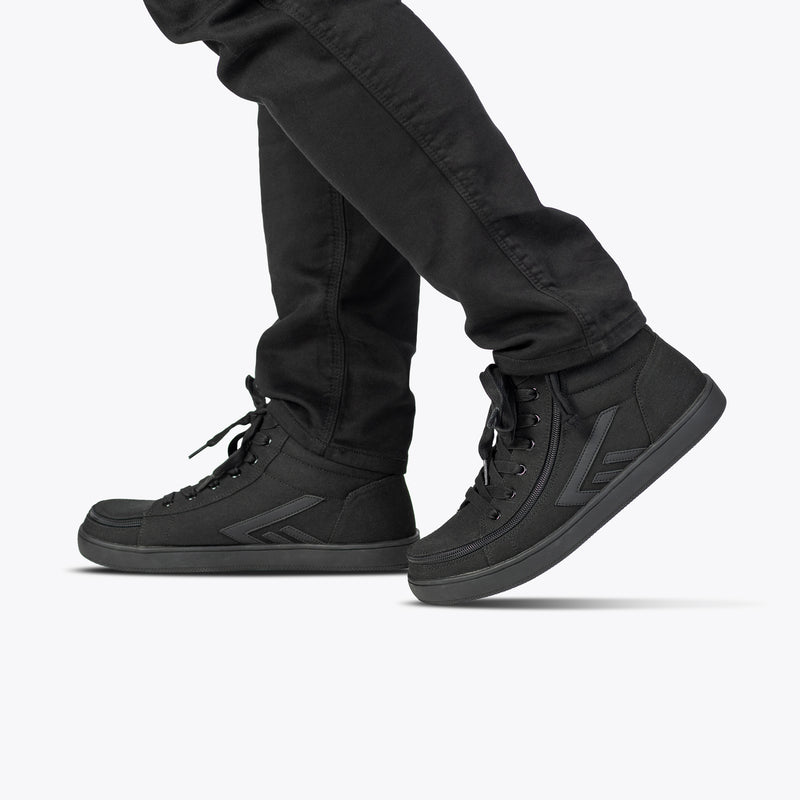 A person in black pants and the Men's Black to the Floor BILLY CS High sneakers by BILLY Footwear, featuring the Full Wrap Zipper design, is walking—shown from the knees down against a plain light background.