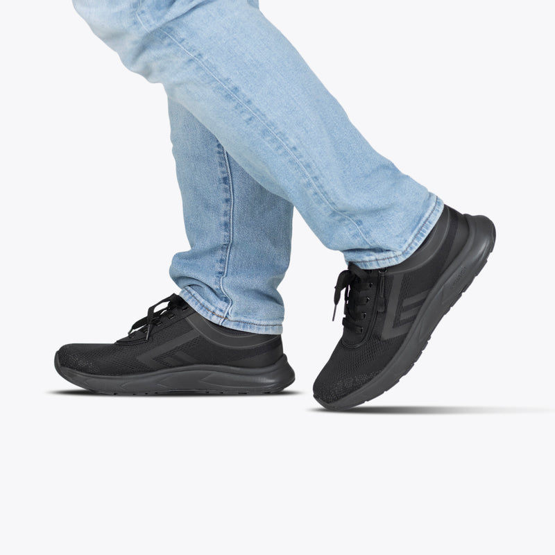 A person is shown from the lower legs down, wearing light blue jeans and Men's Black to the Floor BILLY Sport Inclusion sneakers by BILLY Footwear, walking against a white background.