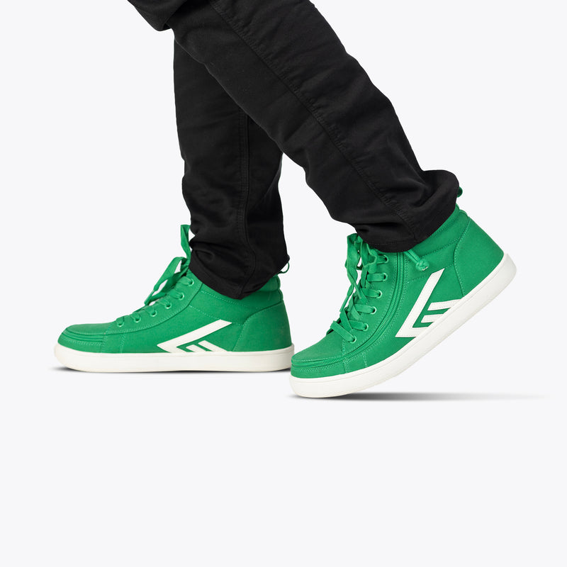 A person in black pants steps forward wearing Men's Green/White BILLY CS High sneakers by BILLY Footwear, featuring white soles and a bold logo, set against a plain white background.