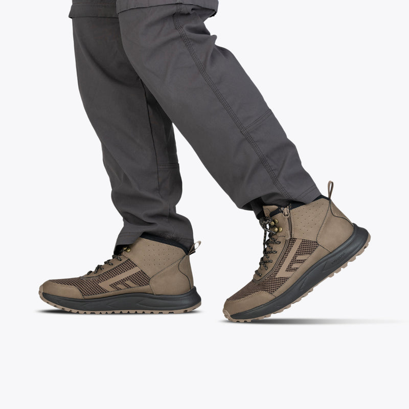 A person wearing gray cargo pants and taupe Men's BILLY Inclusion Trail Boots by BILLY Footwear, featuring an easy on/off zipper, stands against a plain white background.