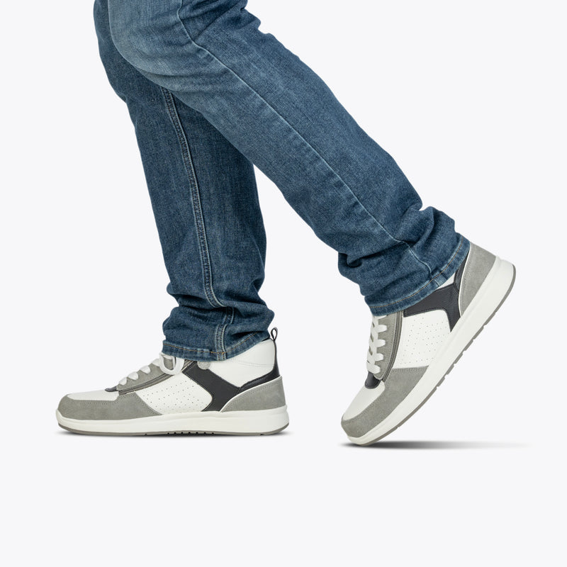 A person in blue jeans and BILLY Footwear Men's White/Grey/Black BILLY Comfort DZ High sneakers is shown walking, one foot lifted off the ground against a plain white background.
