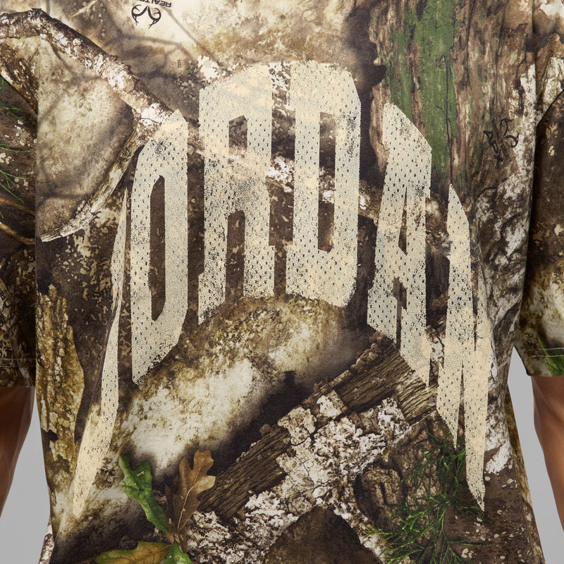 Realtree AOP tee close-up: large white block lettering on camo print