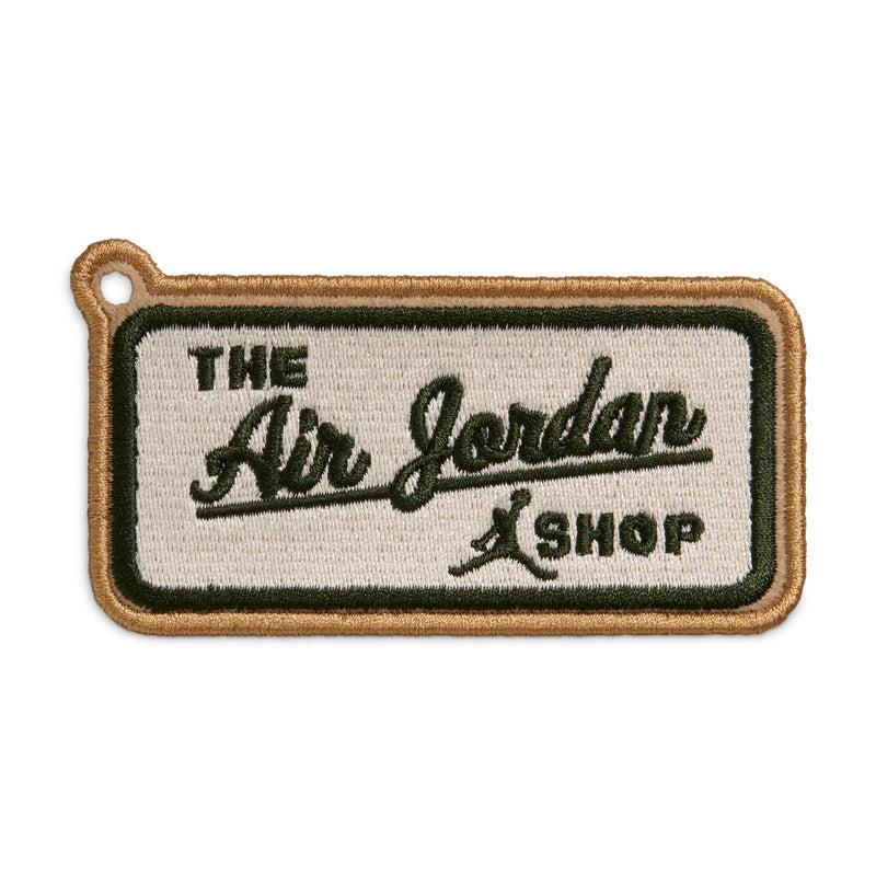 Embroidered patch reading "The Air Jordan Shop" in dark green and tan