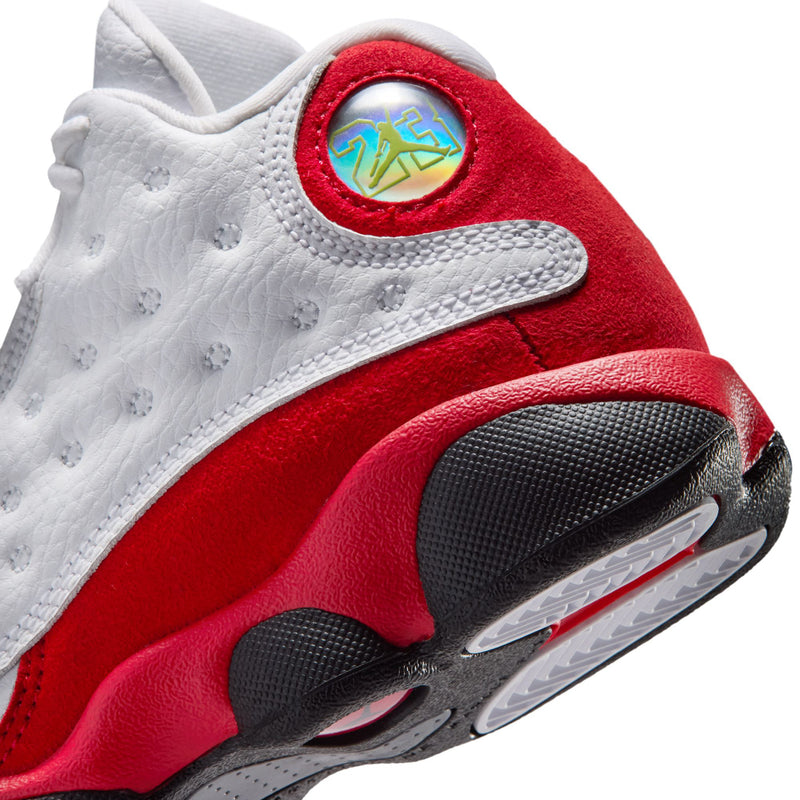 Kids' retro 13 sneaker close-up, red collar with circular logo and black outsole.