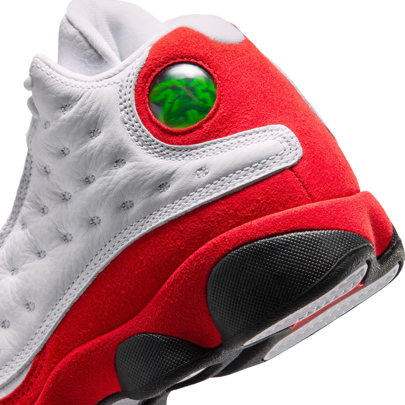 Youth sneaker heel close-up with red suede panel, green badge, and black tread sole