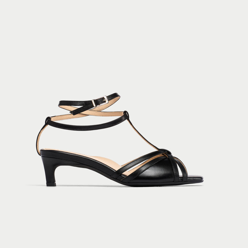 Black sandal with thin straps on a light gray background