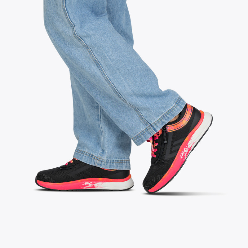 A person in light blue jeans and BILLY Footwear's SALE - Black/Fuchsia Fire BILLY Sport Inclusion shoes walks with one foot lifted and the other flat, set against a plain white background.