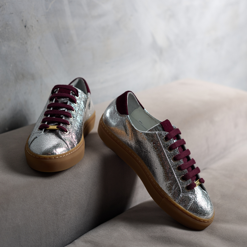 Silver sneakers with maroon laces on a light gray surface