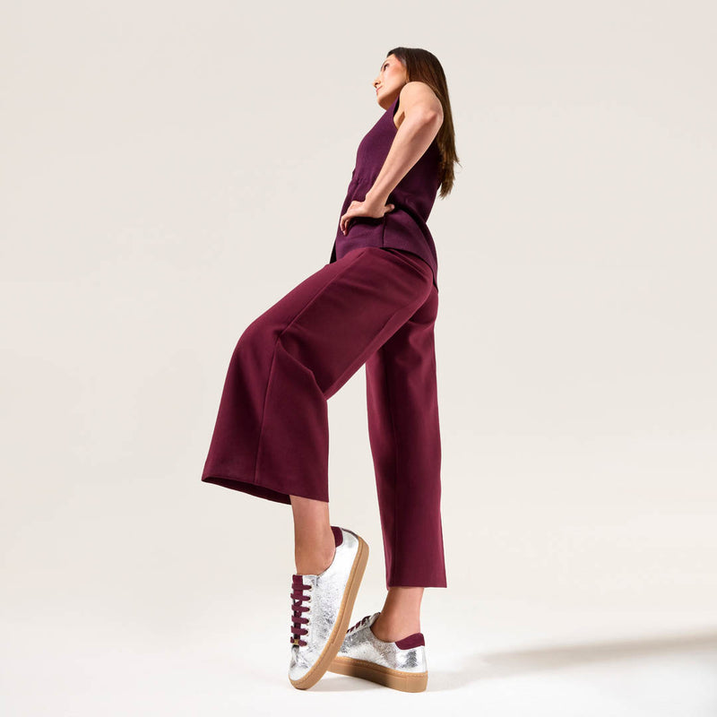 Woman wearing a purple jumpsuit with silver star sneakers on a light background