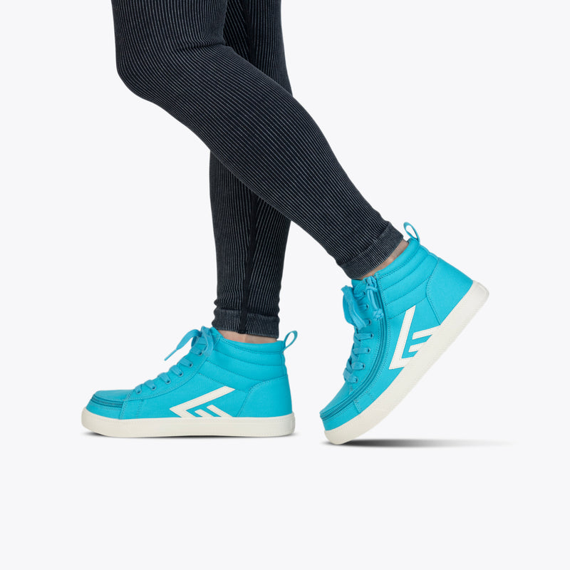 Person in ribbed black leggings and turquoise/white BILLY CS High sneakers by BILLY Footwear, standing on tiptoe against a plain light background—adaptive design with full wrap zipper for easy wear.