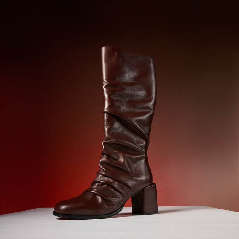 Brown knee-high boot on a white surface with a gradient red background