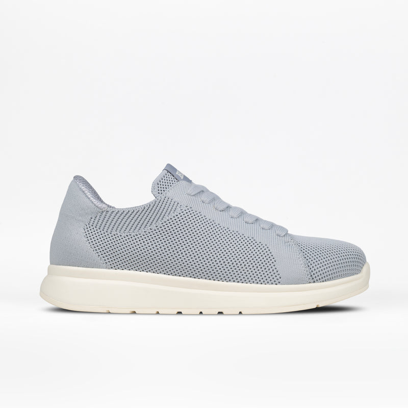 A grey Women's Comfort Knit sneaker by BILLY Footwear with a white sole, shown in profile on a white background. This low-top, breathable shoe features a perforated design and a medial zipper.
